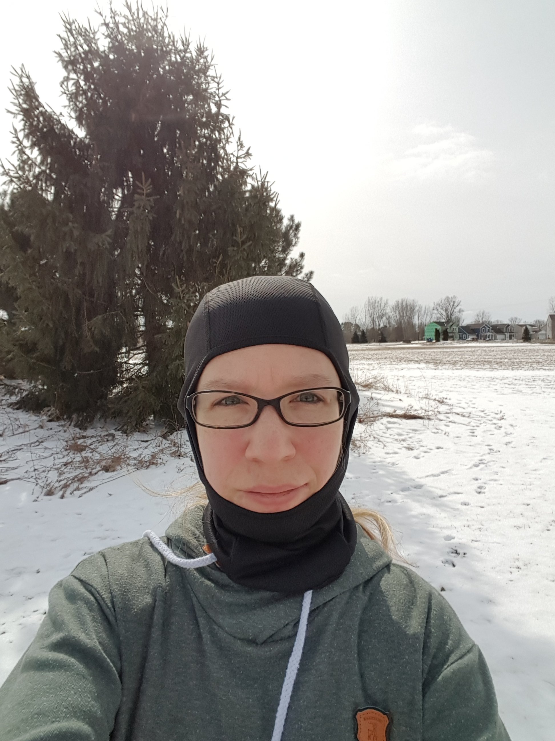 Me, wearing a balaclava on my head, standing in an open field covered in snow. 